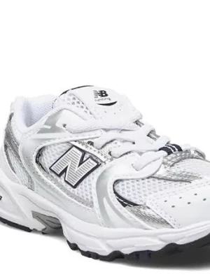 Vita New Balance sneakers med mesh - Stilrena vita sneakers från New Balance med silverdetaljer och svart logga på sidan. Ovandelen är i mesh och syntetmaterial för bra andningsförmåga. Klassisk sportig look med tjock sula och snörning framtill.