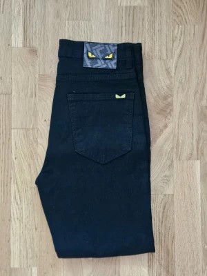 Svarta Fendi jeans - Snygga svarta jeans med raka ben och unika gula ögon-detaljer på bakfickan och linningen. Jeansen har klassisk femficksdesign och är tillverkade i ett stadigt denimtyg. Perfekta för dig som vill sticka ut med coola detaljer.