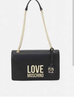Svart handväska från Love Moschino - Stilren svart handväska från Love Moschino med guldfärgade detaljer och kedjerem. Väskan har ett stort LOVE MOSCHINO i guld framtill och en rund logodetalj.  