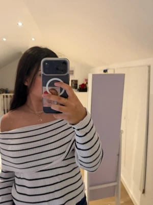 Vit off shoulder stickad tröja - Säljer en vit ribbstickad tröja med svarta horisontella ränder. Tröjan har off shoulder-modell och långa ärmar, vilket ger en trendig och avslappnad look. Perfekt för dig som gillar en stilren och modern vibe.