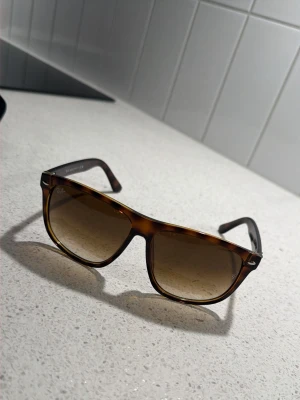 RayBan Boyfriend 4147 - Snygga solglasögon med fyrkantig form och klassiskt sköldpaddsmönster i bruna toner. Bågarna är i plast och glasen är tonade i brunt. Perfekta för soliga dagar och ger en cool retrovibe till din outfit. Storlek 60