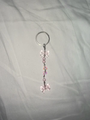 Nyckelring med rosa pärlor och rosetter - (Handgjord) Söt nyckelring med två ljusrosa rosetter, rosa pärlor och små färgglada plastdetaljer. Metallring för enkel fastsättning på nycklar eller väska. Perfekt accessoar för dig som gillar gulliga detaljer💗🎀 Handgjort av mig, perfekt för en gullig outfit! ✨