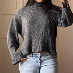 Grå oversized stickad polotröja - Mysig grå stickad polotröja med oversized passform och vida ärmar. Tröjan har ribbstickade detaljer vid nederkant och ärmslut samt en hög krage. Perfekt för kalla dagar och enkel att styla med jeans eller kjol.