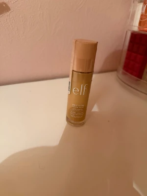 e.l.f. Halo Glow Liquid Filter foundation - e.l.f. Halo Glow Liquid Filter foundation i en beige nyans. Kommer i en cylinderformad glasflaska med beige lock och vit text. Innehåller 31,5 ml (1.06 fl oz) och ger en glowig finish till huden. Aldrig andvänt helt oöppnad 