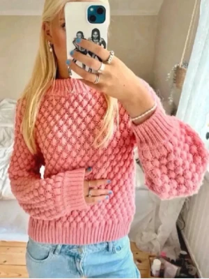 Rosa bubblig stickad tröja - Säljer en superfin rosa stickad tröja med bubbligt strukturmönster och breda ribbade muddar. Tröjan har rund halsringning och ballongärmar som ger en trendig look. Perfekt att matcha med jeans för en avslappnad stil. Storlek M men skulle säga att den även passar S och XS