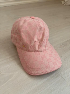 Rosa keps från Gucci med GG-mönster - Snygg rosa keps från Gucci med det klassiska GG-monogrammet över hela kepsen. Kepsen har böjd skärm, justerbar rem bak och är tillverkad i ett slitstarkt tyg med insida i beige bomull. Perfekt accessoar för en trendig och sportig look.