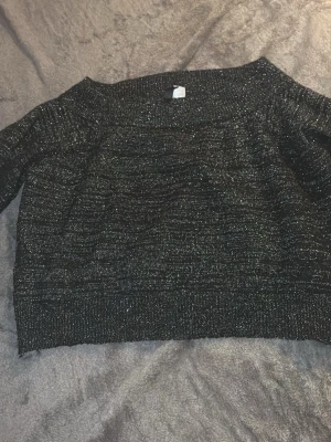 Svart glittrig stickad tröja Divided - Snygg svart stickad tröja från Divided med glittriga inslag. Tröjan har en rak, lite boxig passform och långa ärmar. Perfekt för dig som vill ha något extra till vardagslooken. Materialet är mjukt och stretchigt.