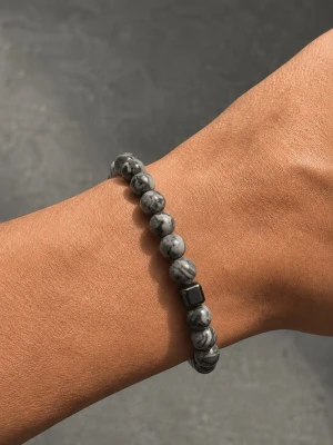 Gråmelerat pärlarmband - Stilrent armband med rundade pärlor i gråmelerad sten och en svart fyrkantig detalj. Elastiskt band som gör det enkelt att ta på och av. Perfekt accessoar för dig som gillar minimalistisk och modern stil.
