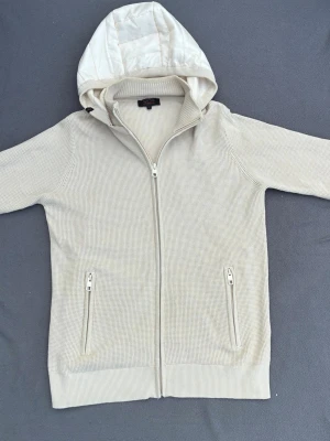 Cardigan med luva - Riktigt snygg beigie cardigan med en clean luva som går att ta av. Storlek L men sitter som M. Passar till det mesta. Rekommenderd längd: 178-188. Mycket fint skick.