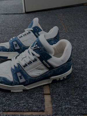 Louis Vuitton blåvita sneakers - Snygga sneakers från Louis Vuitton i blått och vitt med tydliga LV-loggor. Ovandelen är i en mix av denim och läder, med vita snören och detaljer i blått. Skorna har en chunky sula och klassisk siluett som sticker ut.