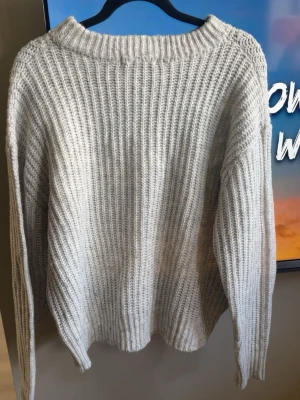 Oversized grå stickad tröja - Mysig oversized stickad tröja i grå med grov ribbstickning och rundad hals. Tröjan har långa ärmar och avslappnad passform, perfekt för lager på lager under kyliga dagar. Materialet känns mjukt och värmande.