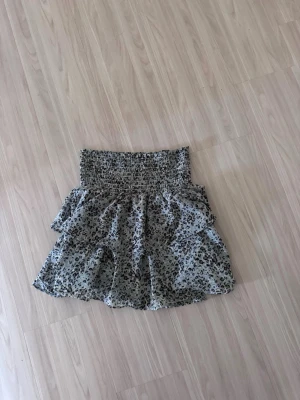 Kort volangkjol med leopardmönster - Söt kort kjol med leopardmönster och volanger. Kjolen har bred smock i midjan för skön passform och är gjord i ett lätt, luftigt material. Perfekt för dig som vill ha en trendig och bekväm kjol med attityd.