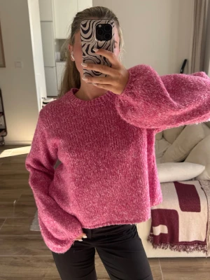 Rosa stickad tröja med ballongärmar - Mysig rosa stickad tröja med breda ballongärmar och rund hals. Tröjan har en mjuk, fluffig struktur och avslappnad passform. Perfekt för att hålla sig varm och ändå se trendig ut. Passar till både jeans och kjol.