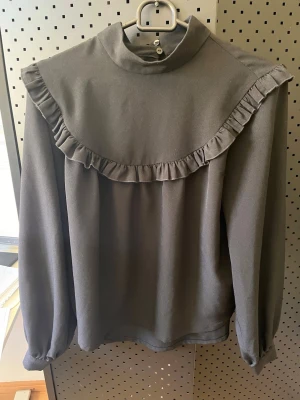 Svart blus Monki strl S volanger  - Svart blus med volanger från Monki strl S. Material: polyester. Mycket fint skick. 