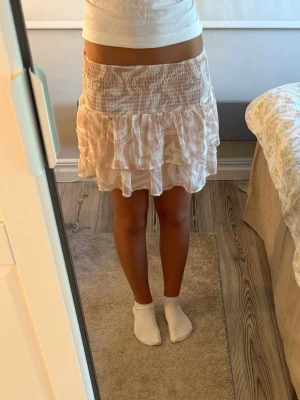 Ljusrosa volangkjol från KappAhl -  kort volangkjol från KappAhl i ljusrosa och vitt med smock i midjan. Kjolen har ett skirt, luftigt tyg och ett diskret randigt mönster.  