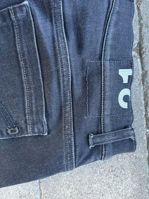 Svarta raka jeans med tryck - Säljer ett par svarta jeans med raka ben och klassiska bakfickor. Jeansen har ett vitt tryck med siffran 5 på linningen och är tillverkade i stretchigt denimtyg. Perfekta för en clean och stilren look.