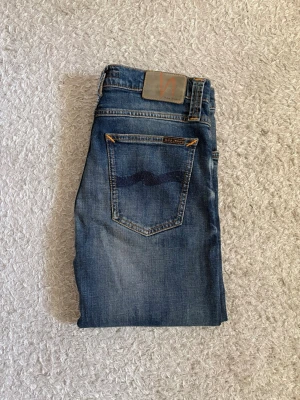Nudie Jeans - W30/L32 - Blå jeans från Nudie Jeans i storlek W30/L32. Jeansen är i nyskick, men inte med prislapp.  Klassiska Nudie-detaljer med broderade bakfickor. Säljs då de är för små för mig. Modellen är slim, High Kai.  📦 Snabb leverans! 💬 Hör gärna av dig vid frågor eller om du vill ha fler bilder/mått!