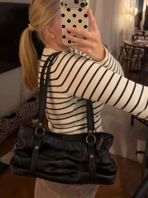 Svart axelväska i skinnimitation - Snygg svart handväska i skinnimitation med dubbla axelband och guldfärgade detaljer. Väskan har en mjuk, rynkad design och dragkedja upptill. Perfekt storlek för att få plats med allt du behöver till dagen❤️🌸🫶🏻