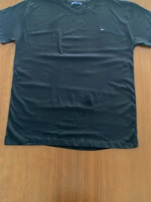Svart t-shirt med liten logga - En stilren svart t-shirt i bomull med liten diskret logga på bröstet. Klassisk passform och rund halsringning, perfekt till jeans eller shorts. Enkel och clean design som funkar till det mesta.