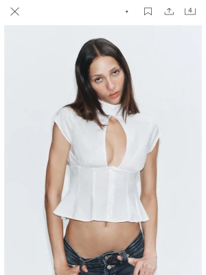 Vit kortärmad blus med cut-out - Trendig vit blus med korta ärmar och en snygg cut-out detalj framtill. Blusen har en figurnära passform, markerad midja och lätt utsvängd nederkant. Stängs med knappar framtill och har en hög krage för en modern look. Perfekt för att lyfta vilken outfit som helst.