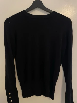 Svart tröja från Zara med knappar - Säljer en svart långärmad tröja från Zara. Tröjan har rund halsringning och dekorativa silverfärgade knappar vid ärmsluten. Enkel och stilren modell som passar till mycket. Materialet känns mjukt och stretchigt.