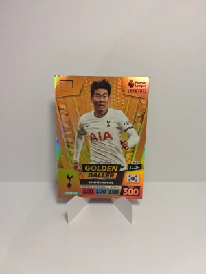 Panini Golden Baller fotbollskort - Säljer ett Panini Premier League Golden Baller samlarkort med Son Heung-Min från Tottenham. Kortet har en glansig guldlook med färgstarka detaljer och visar spelarens position, stats och landsflagga. Perfekt för dig som samlar på fotbollskort eller gillar Premier League.