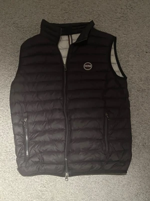 Svart dunväst från Colmar - Snygg svart dunväst från Colmar med quiltad design och två dragkedjeförsedda fickor framtill. Västen har hög krage och Colmar-logga på bröstet. Insidan är ljusgrå vilket ger en schysst kontrast. Perfekt för lager-på-lager och streetwear. Detta är en barn storlek som är 172 cm lång och brukar passa på 16 åringar!!om man tänker på vanliga storlek passar den för en som har xs möjligtvis small. Inte använd så mycket så bra skick ändå!! Säljer för 650 kr kan gå ner till 550 kr!!