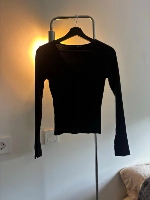 Svart ribbad långärmad topp - Svart ribbad topp med lång ärm och v-ringning. Toppen har en slim passform och är gjord i ett stretchigt material som sitter snyggt på kroppen. Enkel och stilren design som passar till mycket.