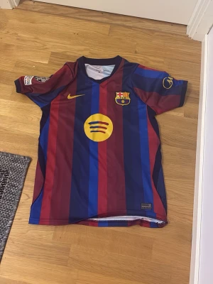 FC Barcelona matchtröja Pedri #8 - Säljer en officiell FC Barcelona matchtröja med Pedri och nummer 8 på ryggen. Tröjan har blå och vinröda vertikala ränder, klubbmärke och Nike-logga på bröstet samt Spotify-logga i gult. Tillverkad i lätt och ventilerande material, perfekt för fotbollsträning.