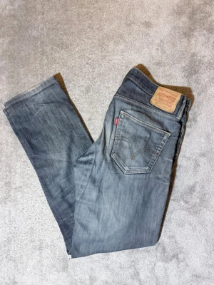 Blå Levi's jeans 511 - Säljer ett par klassiska blå Levi's jeans 511  med snygga slitningar och tvättade detaljer. Jeansen har fem fickor, knappgylf och raka ben. Perfekta för en avslappnad och trendig look. W34 L32.