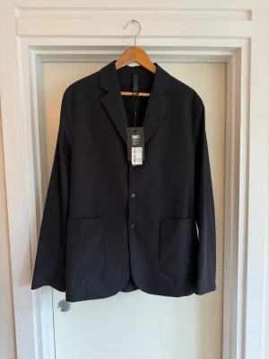 Svart kavaj med två knappar - Stilren svart kavaj med två knappar framtill och två stora fickor. Klassisk krage och enkel design som passar till många olika looks, perfekt för dig som gillar en clean och modern stil.