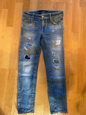 Blå slitna jeans från Jacob Cohën - Säljer ett par blå jeans från Jacob Cohën med slitningar och hål på benen för en cool, avslappnad look. Jeansen har klassisk femficksmodell, knappgylf och är tillverkade i mjukt denimtyg. Perfekta för dig som gillar streetstyle och trendiga detaljer. PRISET ÄR INTE HUGGET I STEN!