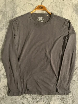 Mörkgrå långärmad T-shirt  - En enkel och stilren mörkgrå långärmad topp i mjukt material. Rund halsringning och normal passform, perfekt att matcha med jeans. Passar dig som gillar minimalistisk stil.