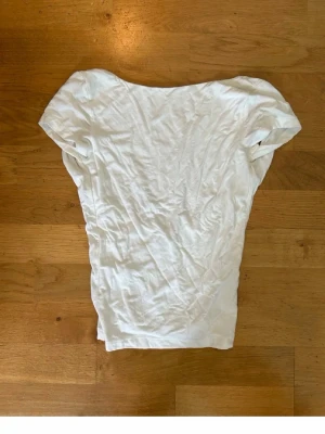 Vit topp med öppen rygg - Säljer en vit topp i mjukt material med korta ärmar och en snyggt öppen rygg. Perfekt för dig som gillar enkel men ändå trendig stil. Passar till många olika outfits och är lätt att matcha.