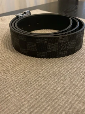 Svart rutigt bälte i skinn - Snyggt svart bälte med rutigt mönster och stilren metallspänne. Bältet kommer med box och påse helt nytt. Pris kan diskuteras och mer bilder