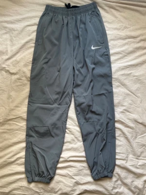 Grå mjukisbyxor från Nike - Säljer ett par grå mjukisbyxor från Nike med resår i midjan och bensluten. Byxorna har en avslappnad passform, sidoficka och den klassiska Nike-loggan på ena benet. Perfekta för chill dagar eller träning.