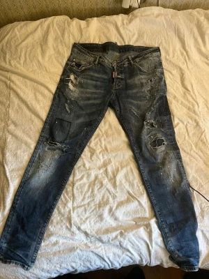 Blå slitna jeans från Dsquared2 - Säljer ett par blå jeans från Dsquared2 med skinny fit och tydliga slitningar, hål och patchdetaljer. Jeansen har klassisk femficksmodell, knappgylf och cool tvätt med ljusa partier. Perfekta för dig som gillar en edgy streetstil.