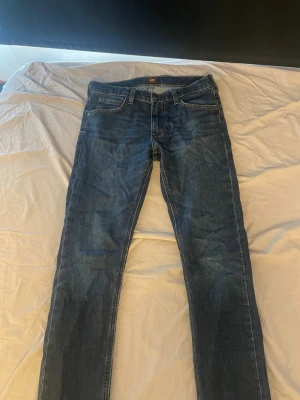 Mörkblå slim fit jeans från Lee - Snygga mörkblå skinny jeans från Lee med klassisk femficksdesign och Lee-lapp bak i midjan. Jeansen har smal passform och är tillverkade i slitstark denim. Perfekta för en trendig och avslappnad stil.