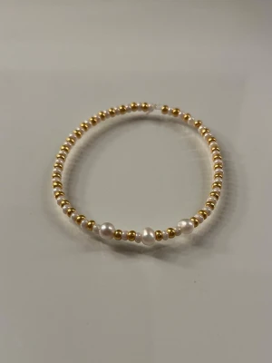 Armband med pärlor och guldfärgade detaljer - Snyggt armband med små guldfärgade pärlor och några större vita pärlor. Armbandet har en enkel och stilren design som passar till många olika stilar. Perfekt accessoar för dig som gillar en elegant touch. Trädd på elastisk tråd för enkel användning.
