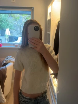 Vit stickad kortärmad tröja - Mysig vit stickad tröja med korta ärmar och rund hals. Tröjan har ribbstickade muddar vid ärmslut och nederkant, och är gjord i ett fluffigt garn som ger en soft känsla. Perfekt att styla med jeans eller kjol för en chill look.
