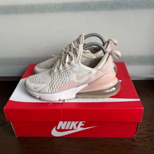 Nike Air Max 270 beige sneakers - Snygga Nike Air Max 270 sneakers i beige och ljusrosa toner med vit sula och genomskinlig Air Max-häl. Ovandelen är i mesh och textil för bra ventilation och komfort. Klassisk snörning och modern design som passar till många stilar.
