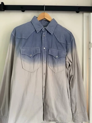 Blåvit skjorta från Isabel Marant - Säljer en snygg blåvit skjorta från Isabel Marant med cool dip dye-effekt. Skjortan har två bröstfickor med knappar, klassisk krage och långa ärmar. Perfekt för dig som vill ha en unik och trendig look.