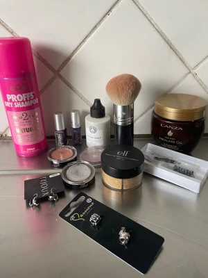 Blandat skönhetspaket med smink & accessoarer - Ett mixat paket med torrschampo, sminkborste, lösögonfransar, ögonskuggor, foundation från e.l.f., nagellack, hårolja från Lanza, örhängen och ansiktsserum. Perfekt för dig som vill testa olika produkter inom skönhet och smink.  Några är halsb såsom Lsnza och ögonskuggor och bluschen 
