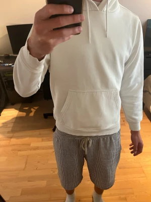 Vit hoodie med magficka och huva - Säljer en stilren vit hoodie med klassisk magficka och dragsko i huvan. Hoodien har ribbade muddar vid ärmslut och nederkant. Perfekt för dig som gillar en clean och enkel look. Passar till det mesta och är superbekväm.