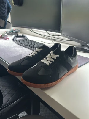Svarta sneakers med brun sula - Stilrena svarta sneakers med vit snörning och brun gummisula. Skorna har en klassisk låg profil och är tillverkade i en mix av läder och syntetmaterial. Perfekta för dig som gillar en clean och tidlös look.