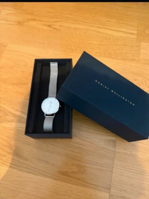 Daniel Wellington klocka - Snygg analog klocka från Daniel Wellington. Använd, men i mycket gott skick. De enda defekter som förekommer är repig baksida (se bilder).   Vattentålig 3ATM Klockglasmaterial: Mineralglas Boett: rostfritt stål Armbandsmaterial: rostfritt stål  Är osäker på måtten då jag förmodligen kortat ner armbandet, men mått från hemsidan finns om man vill jämföra.   uppmätta mått nedan Längd: 21cm Bredd: 1,8cm Diameter ur: 2,8cm  Nypris ca 1500. Hör av er vid frågor/Prisförslag.