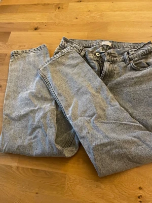 Grå mom jeans med hög midja - Snygga grå mom jeans i klassisk tvätt med hög midja och raka ben. Jeansen har fem fickor, bälteshällor och stängs med knapp och dragkedja. Perfekta för en avslappnad och trendig look.
