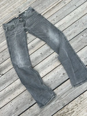 Gråa Replay jeans med raka ben - Säljer ett par gråa jeans från Replay med raka ben och klassisk femficksmodell. Jeansen har en snygg tvättad look och detaljerade sömmar vid fickorna. Perfekta för en avslappnad och trendig stil.