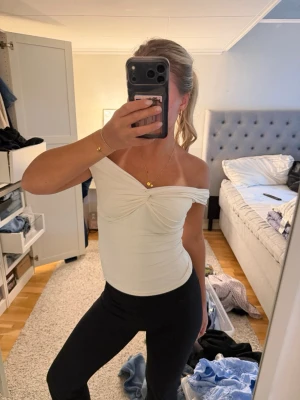 Vit offshoulder topp med twistdetalj - Säljer en snygg vit offshoulder topp med twistad detalj framtill. Toppen är tight och axelbandslös, perfekt för dig som vill ha en stilren och trendig look. Materialet känns mjukt och stretchigt, troligen bomull eller polyesterblandning.