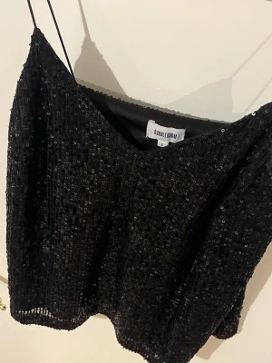 Svart paljettopp från BubbleRoom - Säljer en svart glittrig topp från BubbleRoom med tunna axelband och v-ringning. Toppen är täckt av paljetter som ger ett riktigt snyggt och festligt intryck. Perfekt för dig som vill sticka ut och glänsa lite extra. Pris kan diskuteras vid snabb affär